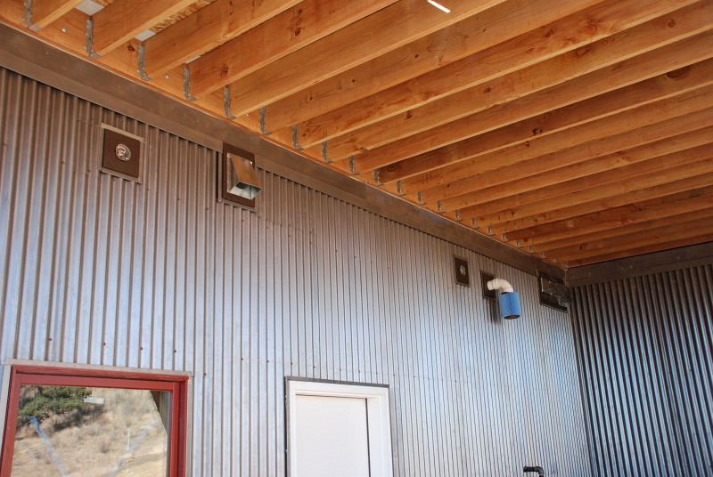 This close up of the east carport shows the 1&frac12;&quot thick cedar pads I built to create a flat surface for the lighting fixtures and ducts that penetrate the corrugated steel. The blue filter is a HEPA vacuum cleaner filter I fitted to the boiler intake to keep construction dust out.